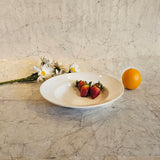 A white ceramic Soup plate with a Vintage Paris design, displayed on a marble surface, accompanied by a small orange and a flower.