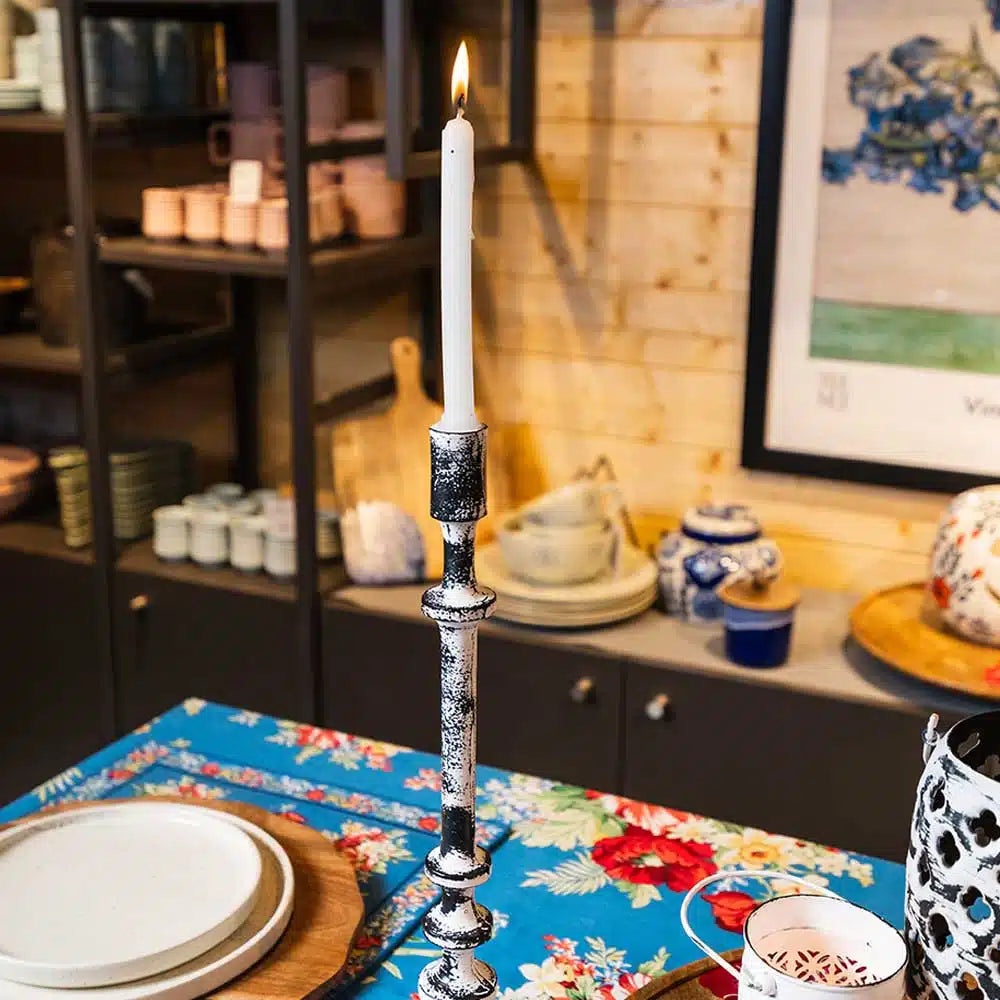 Decorative candlestick with a lit candle on a table.